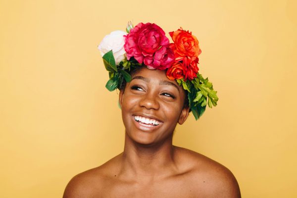 Smiling woman with a floral crown against a yellow background, embodying positivity and excellence